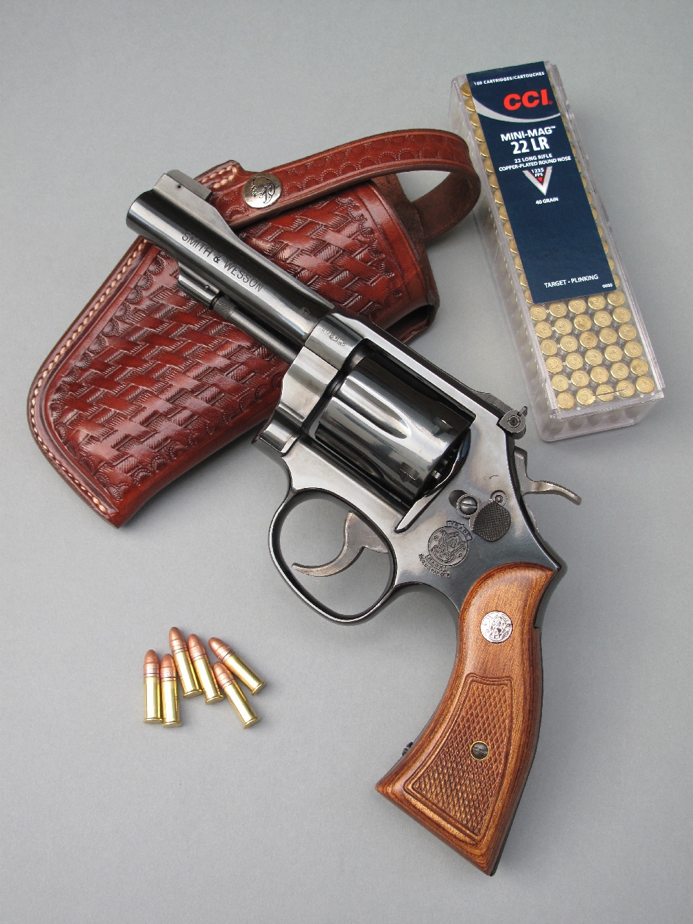 Le Smith & Wesson modèle 18 « Combat Masterpiece », un revolver tout acier de conception traditionnelle, est accompagné ici par une boîte de 100 cartouches de calibre .22 Long Rifle à haute vitesse et par un étui de ceinture en cuir finition basket, réalisé par la maison française La Sellerie du Thymerais, qui reprend l’esprit d’époque des holsters conçus dans les années 1920 par le sheriff et gunfighter Tom Threepersons (1889-1969) et réalisés à El Paso, au Texas, par le sellier Samuel Dale Myres (1871-1953).