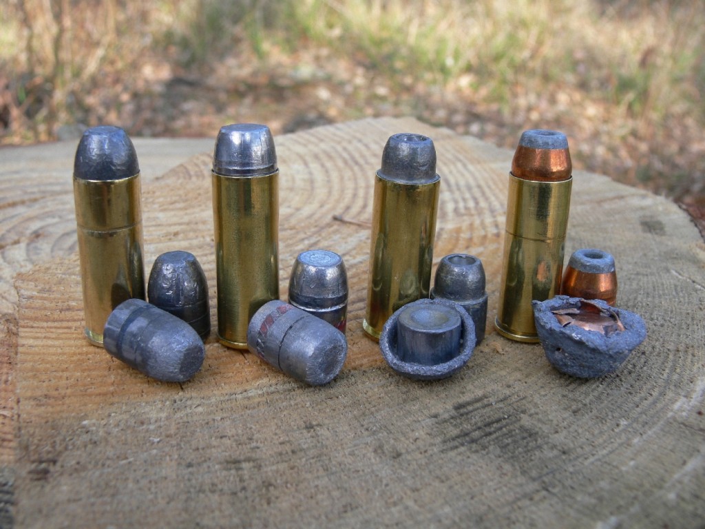 Quatre munitions de calibre .45 Long Colt, accompagnées d’un projectile tiré dans le sable, de gauche à droite : Magtech Cowboy Action à balle en plomb de 250 grains (199 m/s) ; balle Samson semi-wadcutter en plomb de 255 grains rechargée avec 0,40 g de Ba10 (250 m/s) ; Federal Classic à balle en plomb semi-wadcutter expansive de 225 grains (241 m/s) ; balle Sierra Power Jacket demi-blindée expansive de 240 grains rechargée avec 0,70 g de N340 (306 m/s).